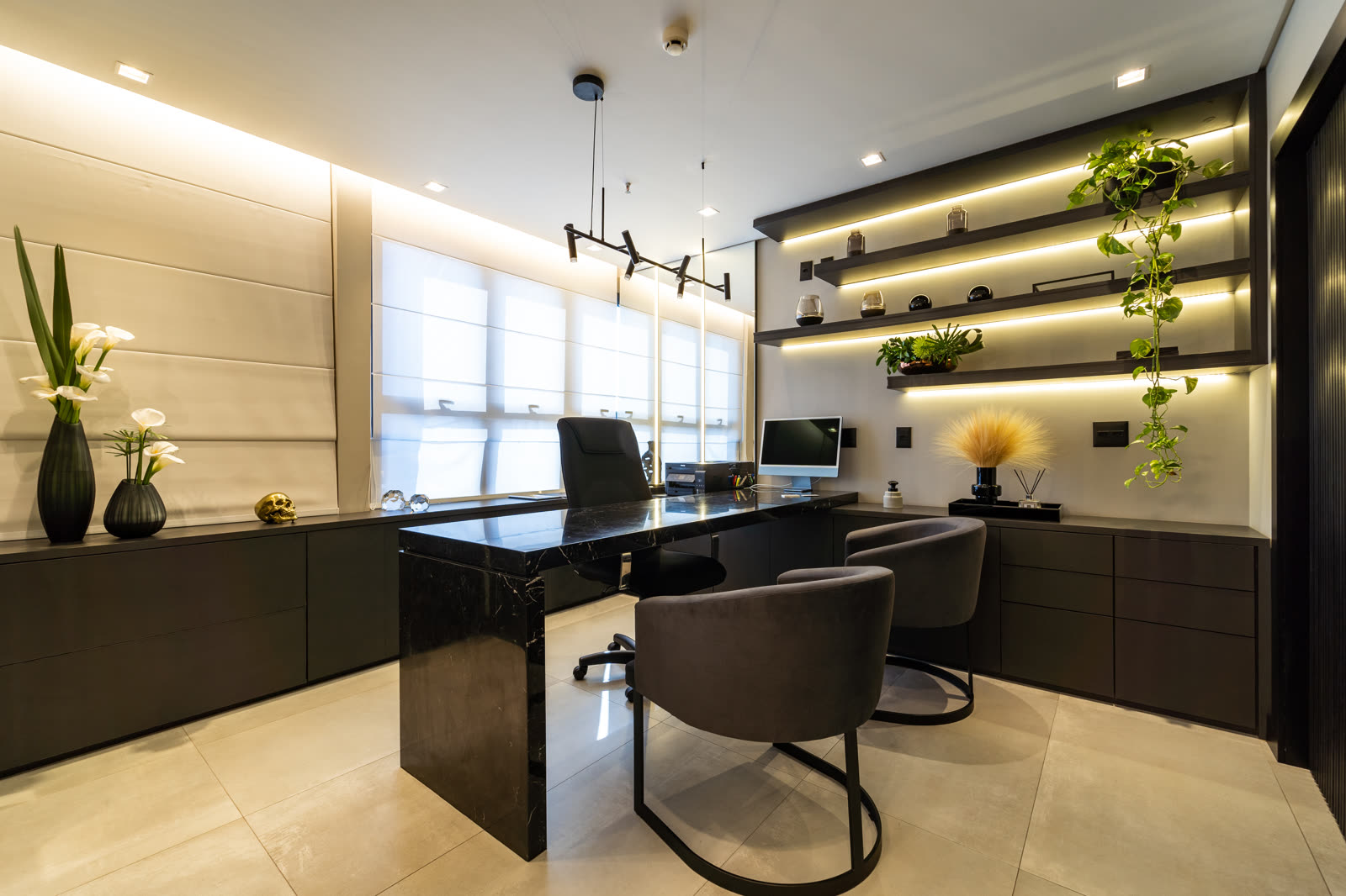Consultório com mesa de atendimento, poltronas e prateleiras iluminadas