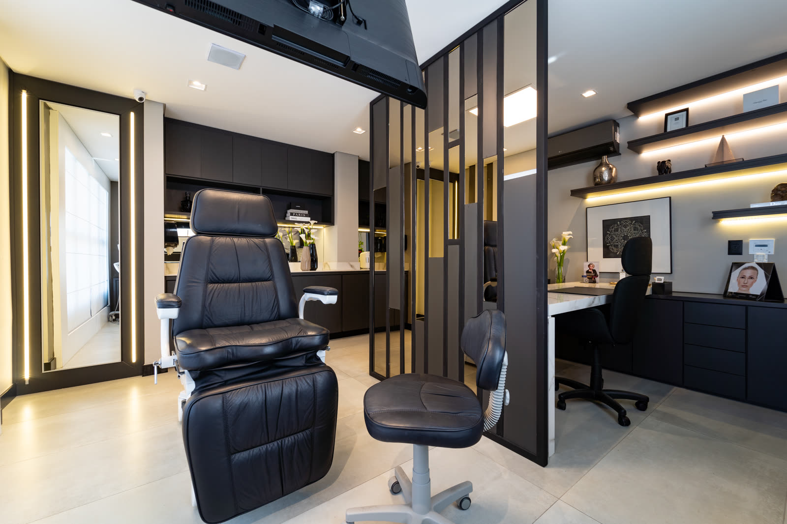 Sala de procedimento do consultório, com poltrona reclinável e prateleiras iluminadas